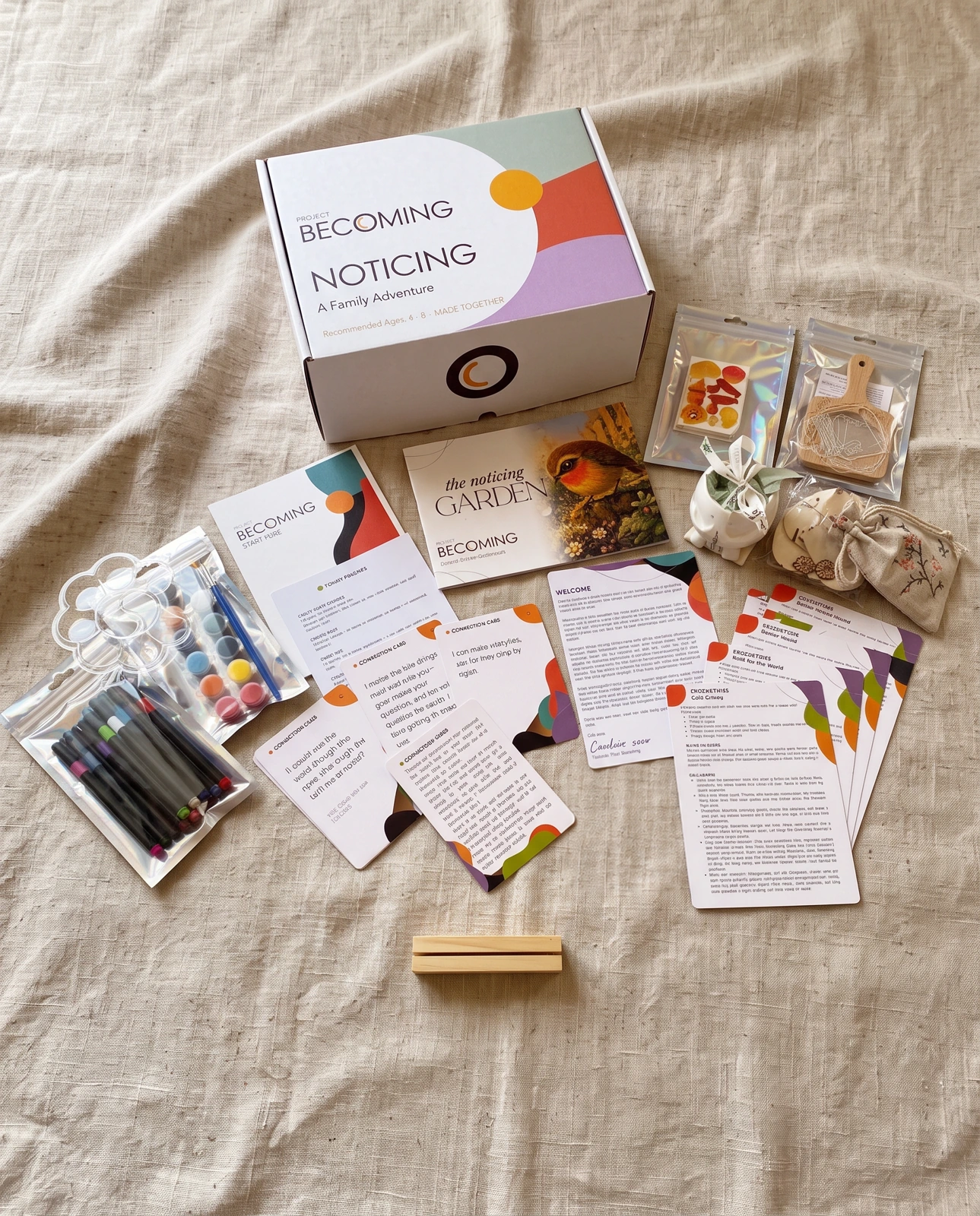 The NOTICING box, picture book, cards and creative materials laid out on natural linen